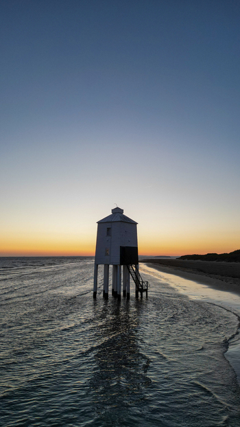 Aerial view of the Burnham on Sea Low Lighthouse standing on wooden stilts on the beach at sunset with calm sea reflecting golden light in Burnham on Sea England United Kingdom. Aerial view of the Burnham on Sea Low Lighthouse standing on wooden stilts on the beach at sunset with calm sea reflecting golden light in Burnham on Sea England United Kingdom.