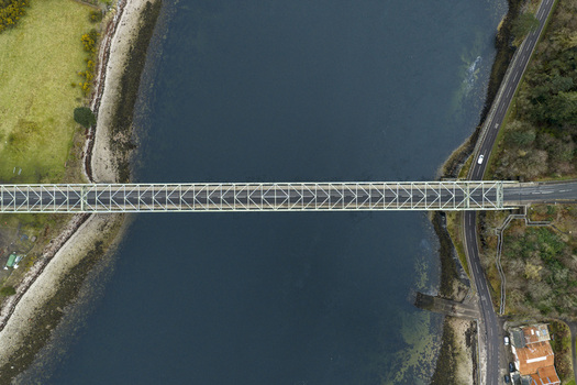 Aerial view of Ballachulish Bridge spanning the dark waters of Loch Leven with surrounding green hills and coastal roads Ballachulish Scotland United Kingdom.
