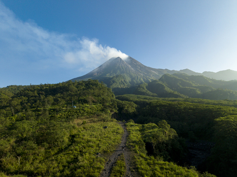 Aerial view of Bunker Kaliadem Merapi and the smoking peak of Mount Merapi surrounded by lush green forests in Kecamatan Pakem Daerah Istimewa Yogya Indonesia. Aerial view of Bunker Kaliadem Merapi and the smoking peak of Mount Merapi surrounded by lush green forests in Kecamatan Pakem Daerah Istimewa Yogya Indonesia.