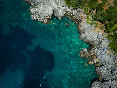 Aerial view of Aquarium Beach featuring turquoise waters and rugged rocky cliffs with lush green vegetation in Jala Vlore County Albania. Aerial view of Aquarium Beach featuring turquoise waters and rugged rocky cliffs with lush green vegetation in Jala Vlore County Albania.