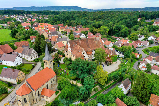 Aerial view of Schloss Wiesenthau and the parish church surrounded by traditional red roofed houses and lush green trees in Wiesenthau Bayern Germany. Aerial view of Schloss Wiesenthau and the parish church surrounded by traditional red roofed houses and lush green trees in Wiesenthau Bayern Germany.