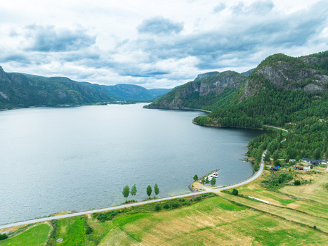 Aerial view of Araksbo lake surrounded by lush green mountains rolling hills and a winding road along the shoreline in Araksbo Agder Norway.