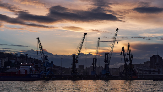 Pasai Donibane Spain 09 March 2026 View of Puerto Pasajes featuring silhouetted industrial cranes and a cargo ship against a dramatic sunset sky with orange clouds. Pasai Donibane Spain 09 March 2026 View of Puerto Pasajes featuring silhouetted industrial cranes and a cargo ship against a dramatic sunset sky with orange clouds.