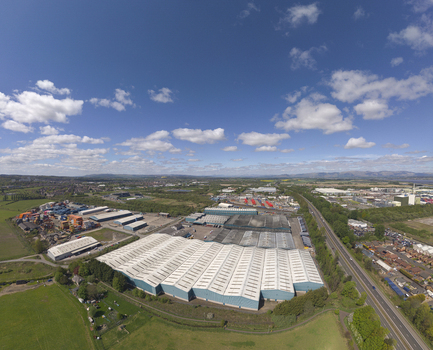 Aerial view of large industrial warehouses and storage facilities surrounded by green fields under a blue sky in Grangemouth Scotland United Kingdom.