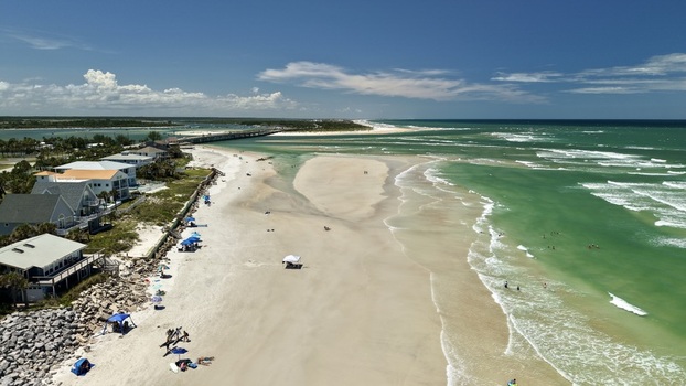 Aerial view of Matanzas Inlet showing the sandy beach coastal homes turquoise ocean water and people relaxing under umbrellas in St. Johns County Florida United States. Aerial view of Matanzas Inlet showing the sandy beach coastal homes turquoise ocean water and people relaxing under umbrellas in St. Johns County Florida United States.