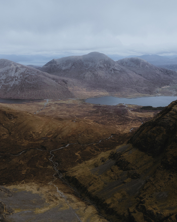 Aerial view of the rugged mountain landscape of Bla Bheinn on the Isle of Skye featuring dramatic rocky peaks and a dark mountain lake in Isle of Skye Scotland United Kingdom. Aerial view of the rugged mountain landscape of Bla Bheinn on the Isle of Skye featuring dramatic rocky peaks and a dark mountain lake in Isle of Skye Scotland United Kingdom.