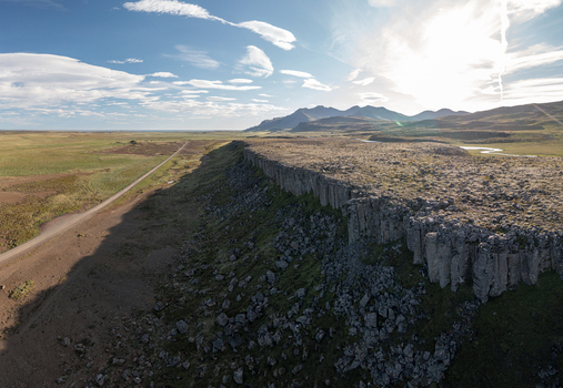 Aerial view of the basalt columns of Gerduberg Cliffs rising above the grassy plains and a dirt road in Raudhamelur Eyja og Miklaholtshr Iceland. Aerial view of the basalt columns of Gerduberg Cliffs rising above the grassy plains and a dirt road in Raudhamelur Eyja og Miklaholtshr Iceland.