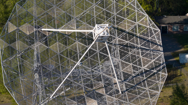 Aerial view of the Dwingeloo Radio Observatory showing the intricate metal lattice of the large parabolic dish surrounded by lush green forest in Dwingeloo Drenthe Netherlands.