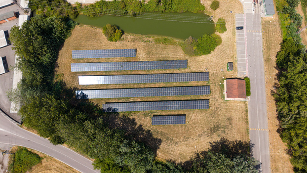 Aerial view of a solar farm with rows of photovoltaic panels a small building and a pond surrounded by trees and a road in Tavazzano con Villavesco Lombardy Italy.