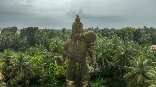 Aerial view of the large stone Hanuman statue holding a mace surrounded by lush tropical palm trees under an overcast sky in Udupi Karnataka India. Aerial view of the large stone Hanuman statue holding a mace surrounded by lush tropical palm trees under an overcast sky in Udupi Karnataka India.