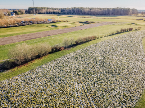 Aerial view of a golf course covered in a light layer of frost with green fairways and surrounding trees in Valmiera Valmiera Latvia.