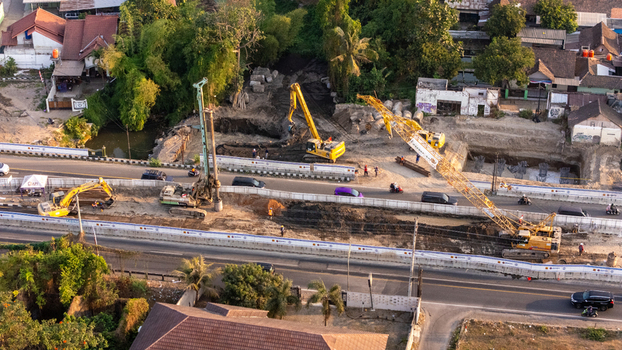 Indonesia 24 September 2026 Aerial view of a construction site with heavy machinery including excavators and a crane working on road infrastructure near residential buildings.