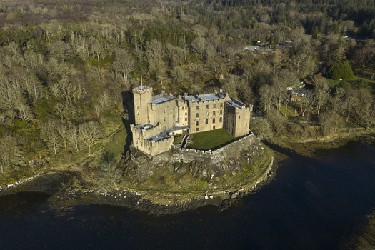 Aerial view of Dunvegan Castle and Gardens situated on a rocky outcrop surrounded by dense woodland and calm water in Isle of Skye Scotland United Kingdom. Aerial view of Dunvegan Castle and Gardens situated on a rocky outcrop surrounded by dense woodland and calm water in Isle of Skye Scotland United Kingdom.