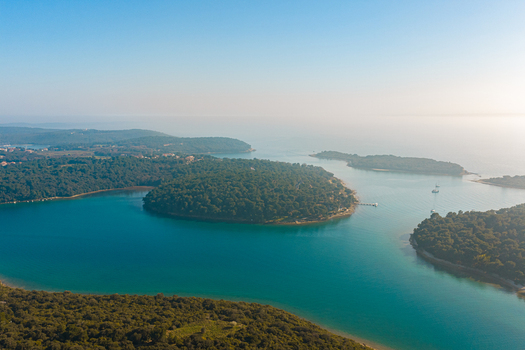 Aerial view of islands embraced by turquoise waters lush green forests and a clear blue sky creating a serene coastal landscape. Pula Istria County Croatia.