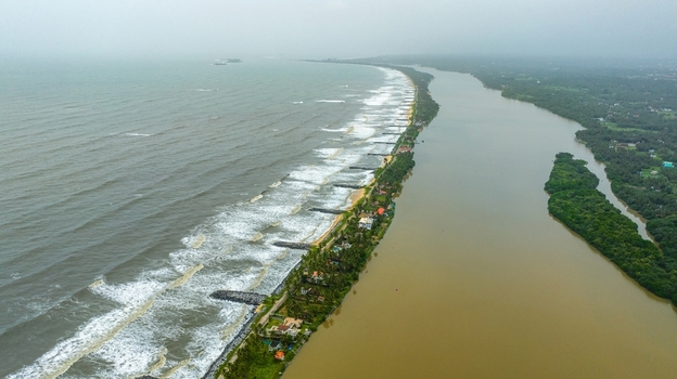 Aerial view of Mattu Beach showing the narrow strip of land separating the Arabian Sea from the backwaters with lush greenery and coastal houses in Udupi Karnataka India.
