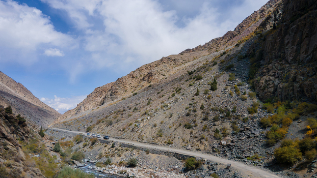 Aerial view of Sadpara Gol mountain road winding through rocky slopes with a river below and cars driving along the path in Skardu Gilgit Pakistan.