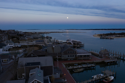 View of Martha s Vineyard with the full moon rising over the historic harbor buildings and wooden docks at twilight in Edgartown Massachusetts United States.