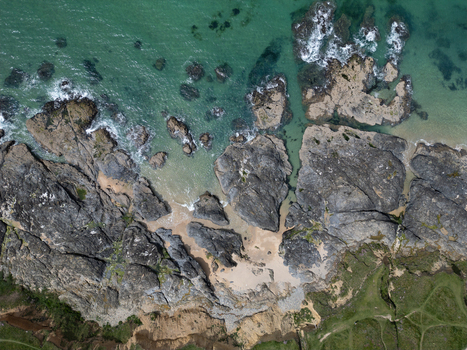 Aerial view of the rocky coastline at Godrevy Beach with dark jagged rocks turquoise sea water and green grassy cliffs in Gwithian England United Kingdom. Aerial view of the rocky coastline at Godrevy Beach with dark jagged rocks turquoise sea water and green grassy cliffs in Gwithian England United Kingdom.