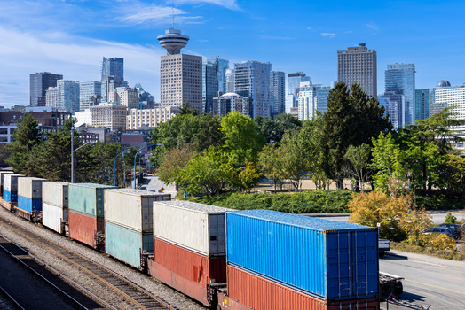 Aerial view of a freight train with colorful shipping containers passing through the urban landscape with the Vancouver skyline and Harbour Centre Vancouver British Columbia Canada.