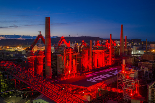 Volklingen Germany 09 May 2026 Aerial view of Volklingen Ironworks illuminated with red lights at dusk featuring tall chimneys and industrial structures under a twilight sky. Volklingen Germany 09 May 2026 Aerial view of Volklingen Ironworks illuminated with red lights at dusk featuring tall chimneys and industrial structures under a twilight sky.