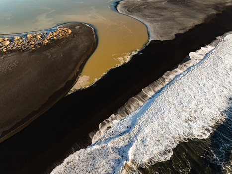 Aerial view of a river flowing into the Atlantic Ocean across a dramatic black sand beach with white crashing surf and volcanic sediment in Reykjanesbaer Iceland. Aerial view of a river flowing into the Atlantic Ocean across a dramatic black sand beach with white crashing surf and volcanic sediment in Reykjanesbaer Iceland.