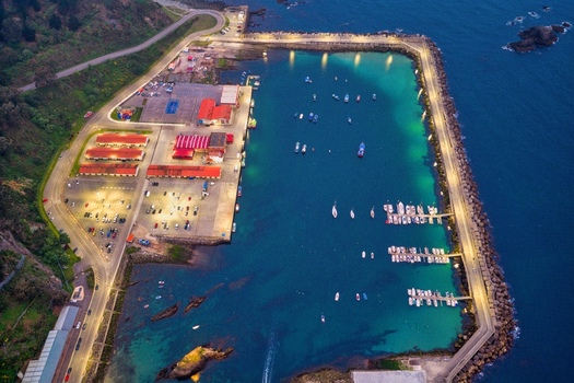 Aerial view of the illuminated port of Cudillero with boats moored in turquoise water and a long breakwater at dusk Cudillero Asturias Spain. Aerial view of the illuminated port of Cudillero with boats moored in turquoise water and a long breakwater at dusk Cudillero Asturias Spain.