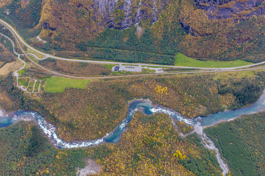 Aerial view of a winding river flowing through a lush forest landscape with a road running alongside in the mountains near Andalsnes More og Romsdal Norway. Aerial view of a winding river flowing through a lush forest landscape with a road running alongside in the mountains near Andalsnes More og Romsdal Norway.