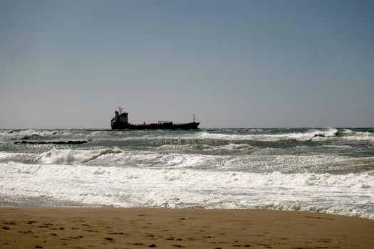 View of a cargo ship sailing on the wavy Mediterranean Sea with a sandy beach in the foreground in Mallorca Balearic Islands Spain.