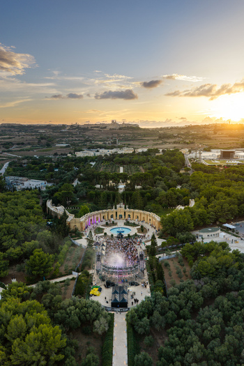 Aerial view of Park Nazzjonali Ta Qali with an outdoor event stage and crowd near the fountain surrounded by trees and Mediterranean landscape at sunset in Attard Northern Region Malta. Aerial view of Park Nazzjonali Ta Qali with an outdoor event stage and crowd near the fountain surrounded by trees and Mediterranean landscape at sunset in Attard Northern Region Malta.