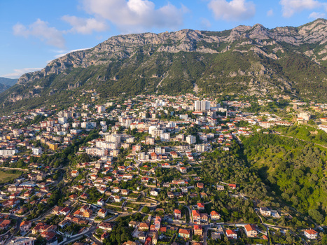 Aerial view of a historic town nestled at the base of a rugged mountain range with red roofed houses and lush green hillsides under a clear sky in Kruje Durres County Albania.