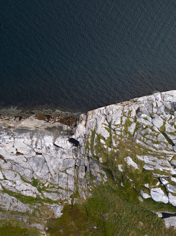 Aerial view of the rugged rocky coastline of Rorvikstranda with dark blue sea water and green mossy patches in Henningsvaer Nordland Norway.