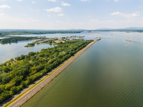 Aerial view of the Danube river with a hydroelectric dam lush green forests and a cargo ship under a blue sky in Bratislava Bratislava Region Slovakia. Aerial view of the Danube river with a hydroelectric dam lush green forests and a cargo ship under a blue sky in Bratislava Bratislava Region Slovakia.