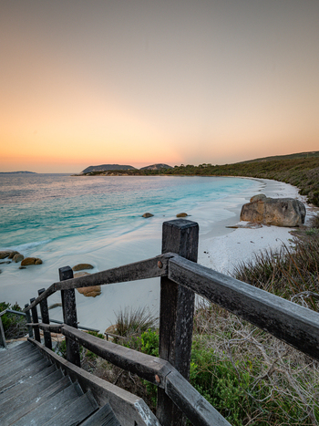 View of Frenchman Bay with wooden stairs leading to the white sand beach turquoise water and granite boulders under a sunset sky in Frenchman Bay Western Australia Australia. View of Frenchman Bay with wooden stairs leading to the white sand beach turquoise water and granite boulders under a sunset sky in Frenchman Bay Western Australia Australia.