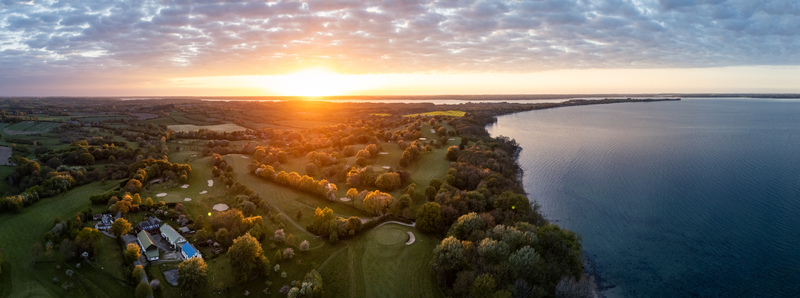 Aerial view of Bockholmwik golf course along the coastline with lush green fairways and trees under a golden sunset Munkbrarup Schleswig Holstein Germany.