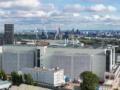 Aerial view of a large modern data center facility with industrial cooling units on the roof surrounded by construction cranes and an urban skyline in the United Kingdom. Aerial view of a large modern data center facility with industrial cooling units on the roof surrounded by construction cranes and an urban skyline in the United Kingdom.