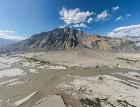 Aerial view of the Shigar River flowing through a vast arid mountain landscape with sandy riverbanks and rugged peaks under a clear blue sky in Skardu Gilgit Pakistan.