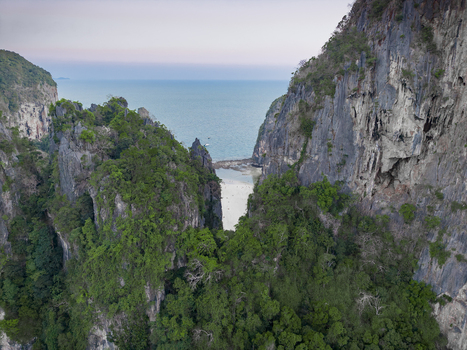 Aerial view of rugged limestone cliffs embrace the turquoise sea vibrant greenery clinging to the rocks creating a dramatic contrast Krabi Thailand.