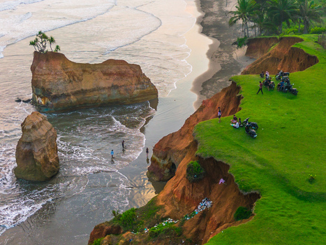 Aerial view of dramatic coastal cliffs with sea stacks lush green grass and people with motorcycles parked on the edge overlooking the ocean in Bali Bali Indonesia. Aerial view of dramatic coastal cliffs with sea stacks lush green grass and people with motorcycles parked on the edge overlooking the ocean in Bali Bali Indonesia.