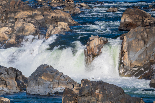 View of powerful rushing water cascading over rugged sunlit rocks creating a dramatic display of nature s force and beauty Great Falls National Park Virginia United States. View of powerful rushing water cascading over rugged sunlit rocks creating a dramatic display of nature s force and beauty Great Falls National Park Virginia United States.