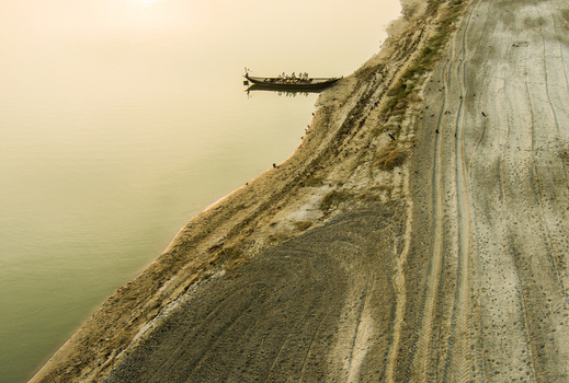 Aerial view of a wooden boat moored on the sandy banks of the Padma River with tire tracks on the shore and calm water in Rajshahi Rajshahi Division Bangladesh.