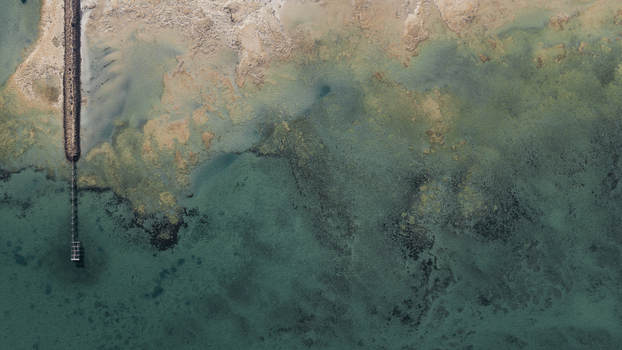 Aerial view of turquoise waters and intricate sand patterns near the shoreline with a long wooden jetty extending into the sea in Denham Western Australia Australia. Aerial view of turquoise waters and intricate sand patterns near the shoreline with a long wooden jetty extending into the sea in Denham Western Australia Australia.