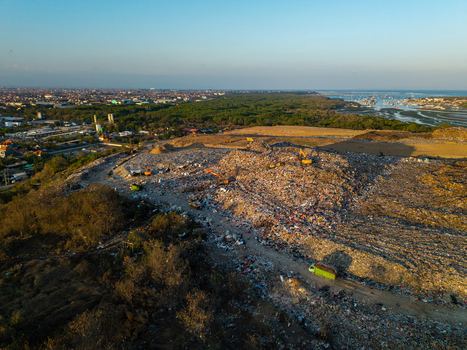Aerial view of TPA Suwung landfill with excavators working on large waste piles surrounded by mangrove forests and urban landscape in Kecamatan Denpasar Selatan Bali Indonesia.