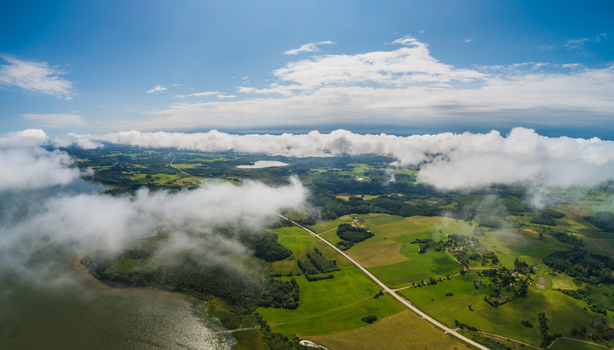 Aerial view of green fields a winding road and a lake under a cloudy sky in Latvia. Aerial view of green fields a winding road and a lake under a cloudy sky in Latvia.