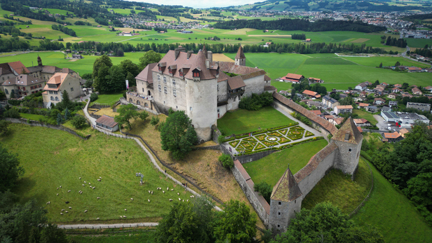Aerial view of the medieval Gruy&egrave;res Castle standing majestically against the backdrop of lush green fields and distant mountains Gruy&egrave;res Fribourg Switzerland.