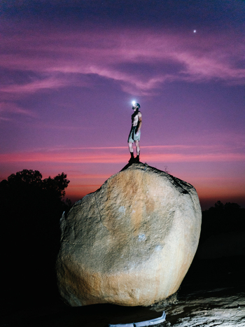 View of a man wearing a headlamp standing on a large granite boulder during twilight in Hampi Karnataka India. View of a man wearing a headlamp standing on a large granite boulder during twilight in Hampi Karnataka India.