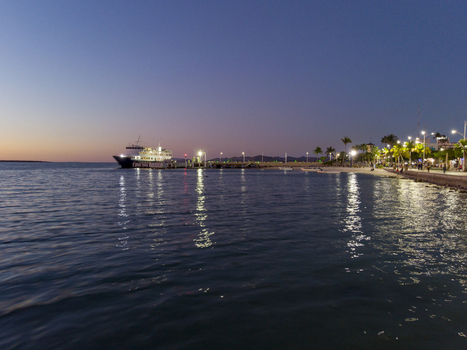 Aerial view of Malecon de La Paz at dusk with a ferry docked at the pier illuminated palm trees and street lights reflecting on the calm water in La Paz Baja California Sur Mexico.