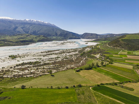 Aerial view of Vjosa Wild River National Park with braided riverbed green fields and snow capped mountains in Permet Gjirokaster County Albania. Aerial view of Vjosa Wild River National Park with braided riverbed green fields and snow capped mountains in Permet Gjirokaster County Albania.