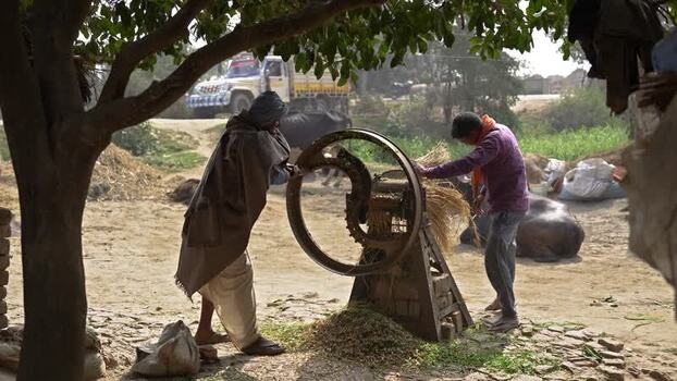 View of men using a manual fodder cutter in rural Patna India.