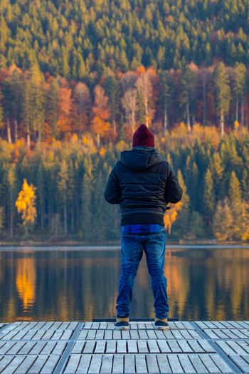 View of a man standing on a wooden pier looking at a calm lake and a dense forest with colorful autumn foliage Breitnau Baden Wurttemberg Germany. View of a man standing on a wooden pier looking at a calm lake and a dense forest with colorful autumn foliage Breitnau Baden Wurttemberg Germany.
