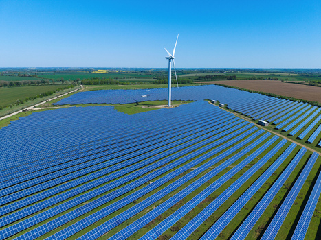Aerial view of Chelveston Wind Farm featuring a wind turbine and vast solar panel arrays under a clear blue sky Wellingborough England United Kingdom. Aerial view of Chelveston Wind Farm featuring a wind turbine and vast solar panel arrays under a clear blue sky Wellingborough England United Kingdom.
